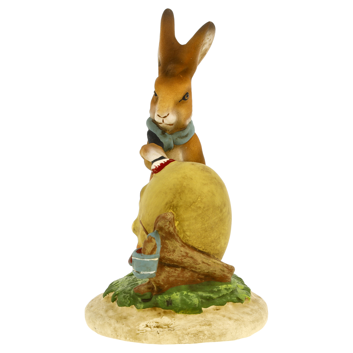 Osterhase-Figur bemalt ein großes Ei mit Pinsel; kleines Eimerchen und Baumstamm auf grünem Sockel, braun-gelb, detailreich